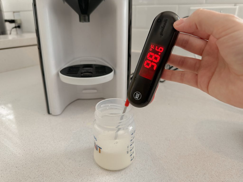 Person holding thermometer measuring 98.6 degrees of formula