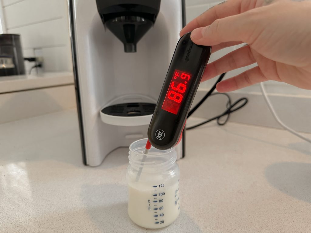 Person holding thermometer measuring 86.9 degrees of formula