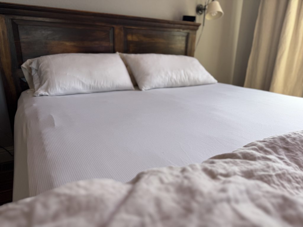 Cozy Earth Bamboo Sheet Set shown on a bed against a wooden headboard.