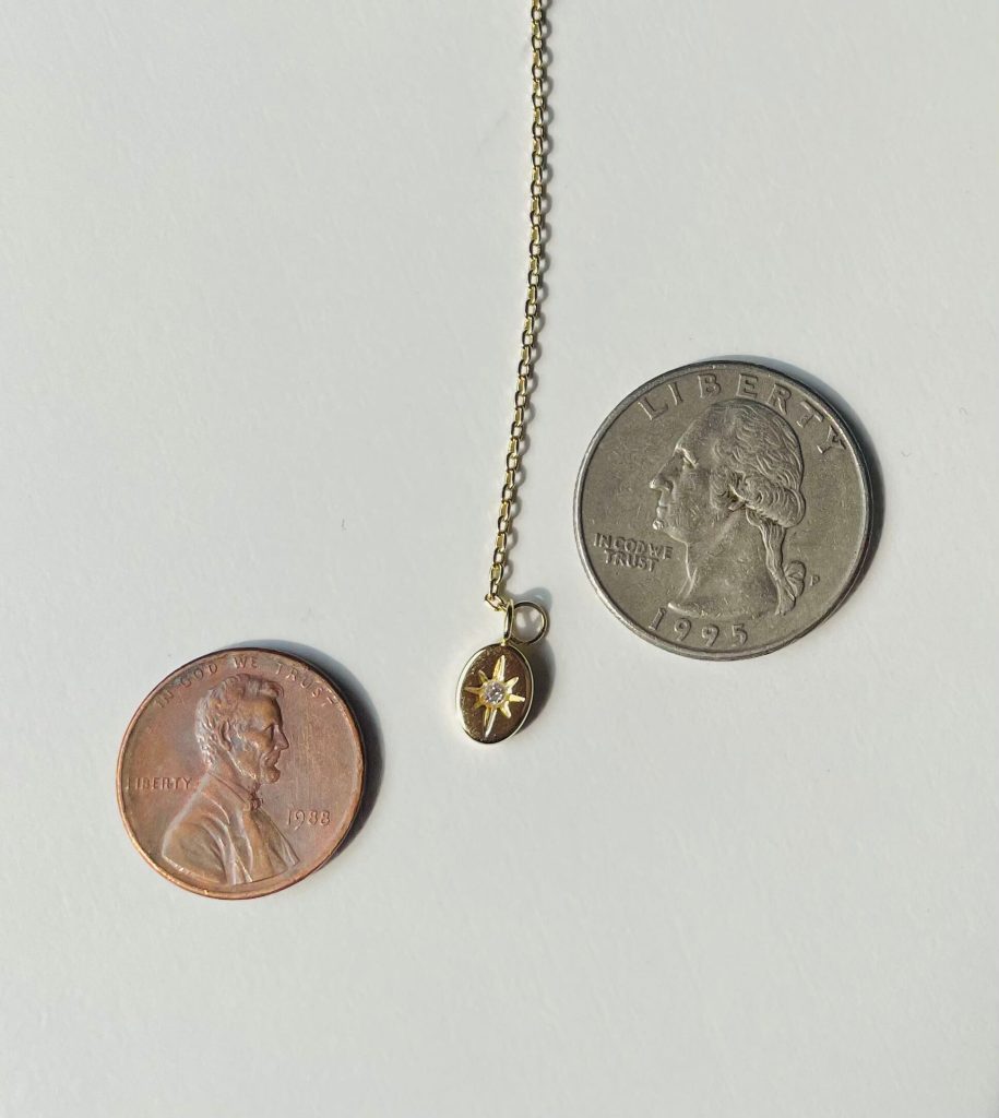 The Pavoi North Star Necklace is between a penny and quarter to illustrate how small it is.