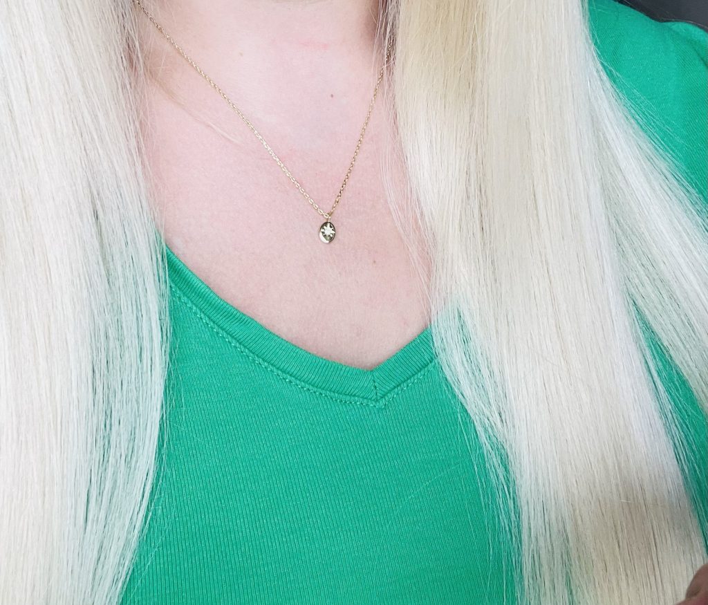 Woman wearing a green v-neck top and a small gold pendant necklace