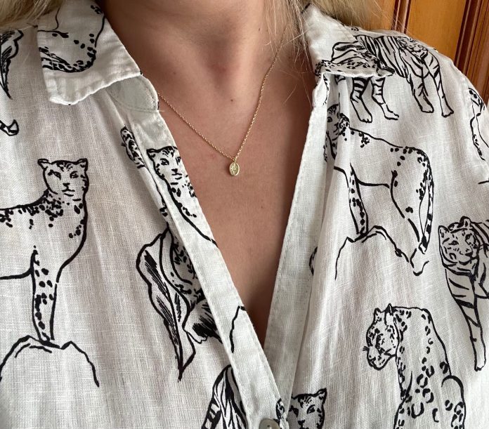 Woman wearing a black and white button-down shirt with big cats and wearing a pendant necklace