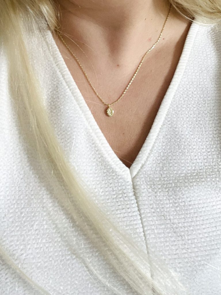 A woman wearing a v-neck top and a small gold pendant necklace.